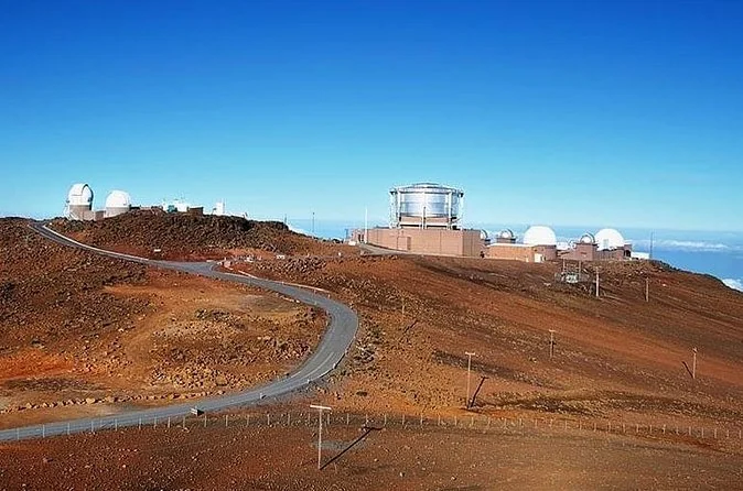 The summit road curving up a bare red cinder slope to the white observatory domes under a blue sky