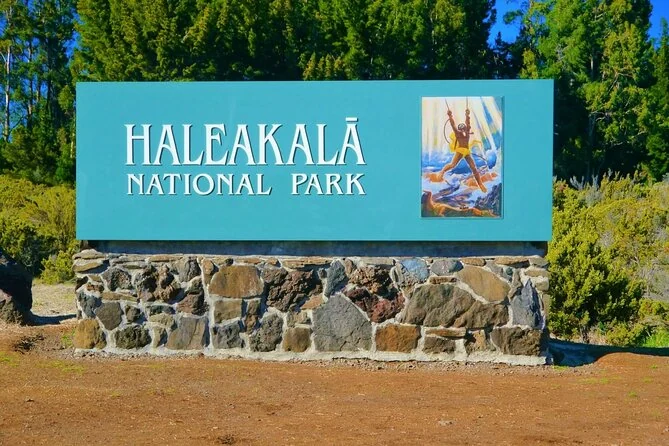 The blue Haleakala National Park sign on a stone wall beside the road, with trees behind