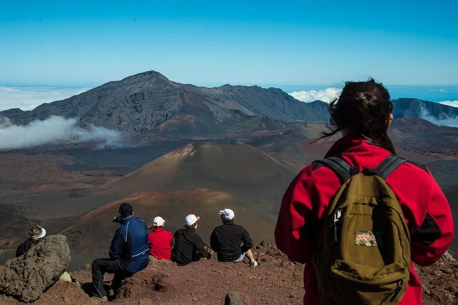 Hikers from behind, one with a red backpack, looking out over the crater floor and its cinder cones