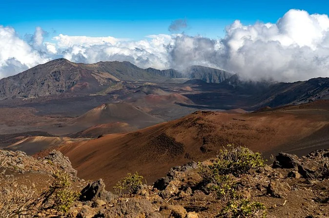The crater floor with red and brown cinder cones and clouds pouring over the far rim