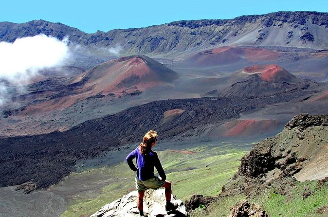 A hiker standing on a rock at the crater rim, small against the cinder cones and the far wall