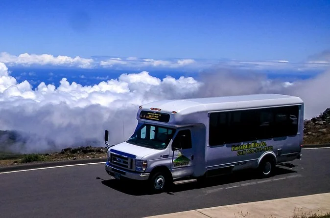 A tour minibus climbing the switchbacks of the Haleakala summit road above the clouds