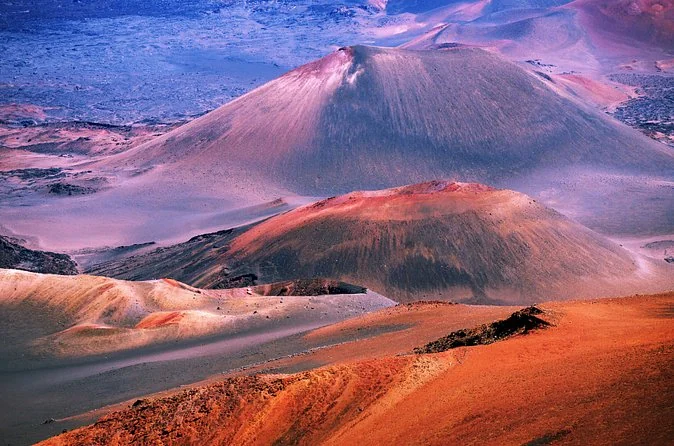 Pink and red cinder cones on the crater floor under a pale sky