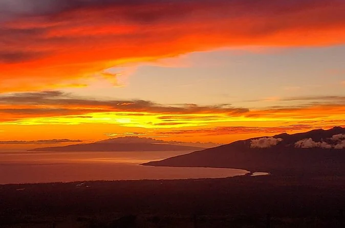 A deep red and orange sunset over the clouds, with the West Maui mountains and the isthmus below