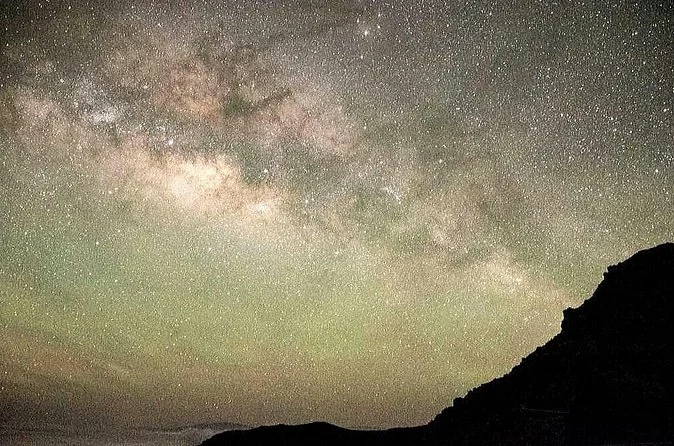 The Milky Way in a dense band of stars above a dark mountain silhouette